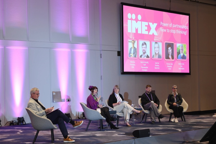 Four speakers and a moderator on stage during IMEX