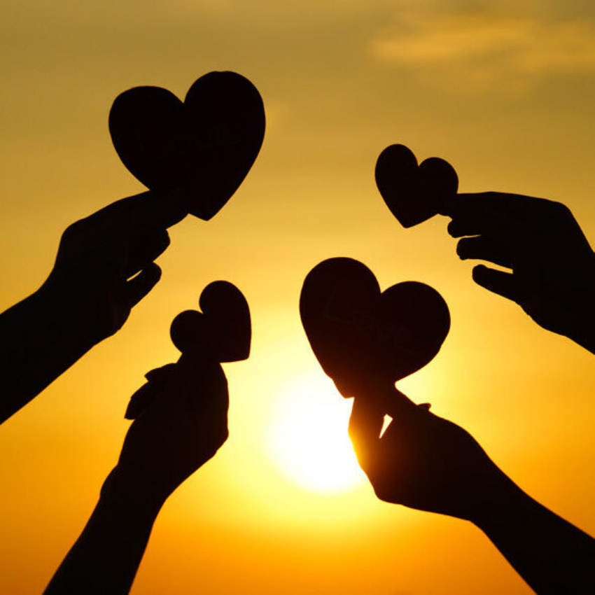 Four hands holding heart shapes in front of the sunlight