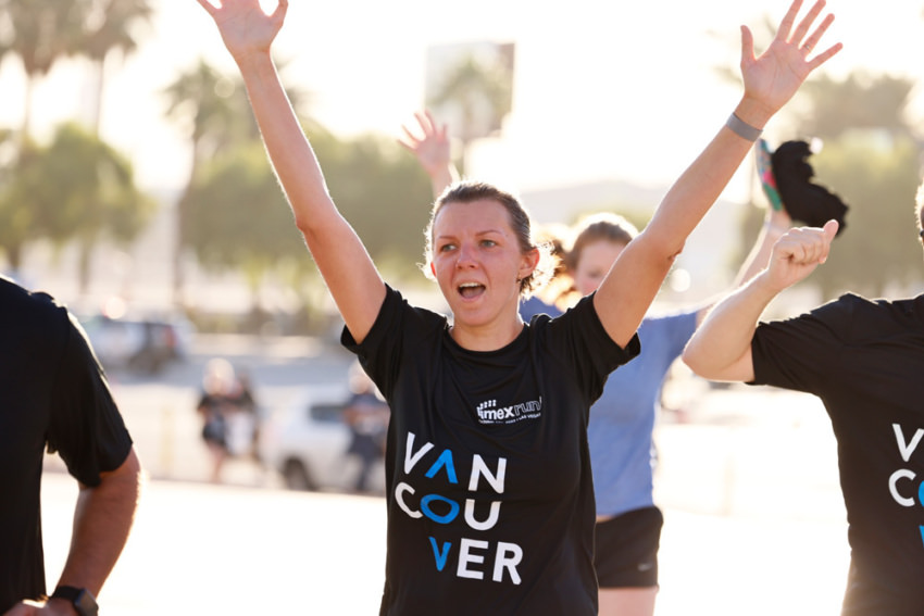 Woman with black tshirt and hands in the air at the IMEX run finish line