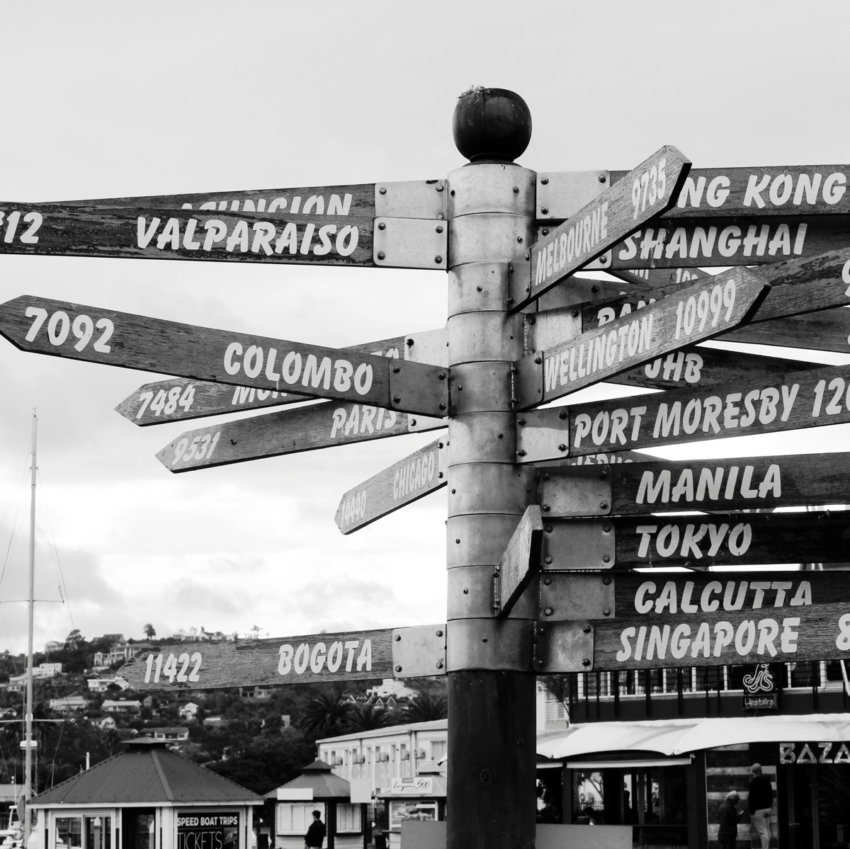Signs on a pole pointing to various countries with the mileage distance